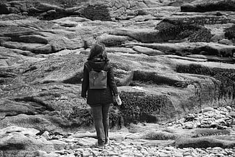 Woman walking on rocky coastal landscape in black and white