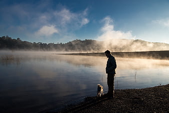 Man and Dog Standing by Misty Lake at Sunrise