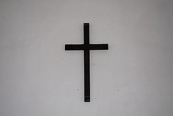 Simple black wooden cross on white wall background