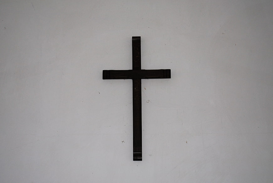 Simple black wooden cross on white wall background