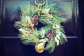 Christmas wreath with pine cones and gold bell on dark door