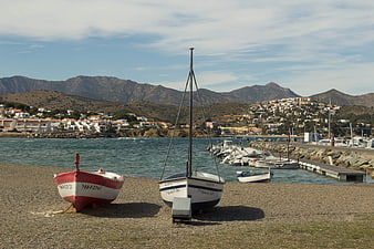 Fishing boats on pebble beach with coastal village and mountains