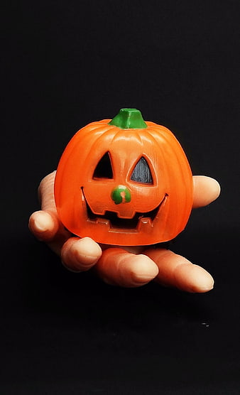 Hand holding orange plastic jack-o'-lantern toy on black background