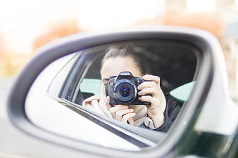 Woman taking photo in car side mirror reflection