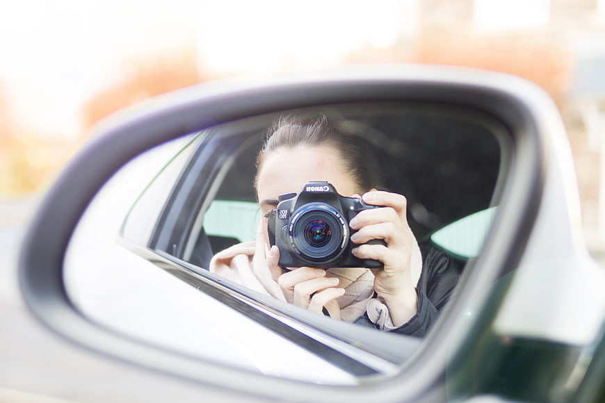 Woman taking photo in car side mirror reflection