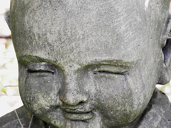 Close-up of weathered stone Buddha statue face with moss