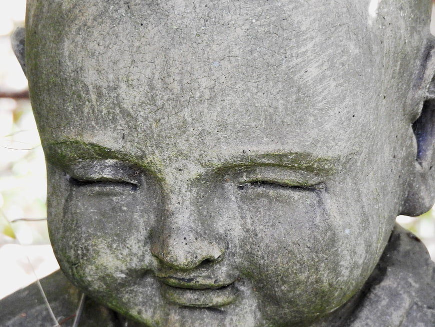 Close-up of weathered stone Buddha statue face with moss