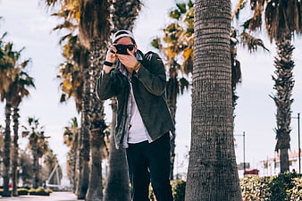 Man taking photo with camera among palm trees outdoors