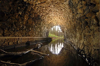 Ancient stone tunnel with water channel and forest exit