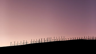 Silhouette of wind turbines on a hill against a purple sunset sky