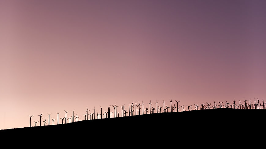 Silhouette of wind turbines on a hill against a purple sunset sky