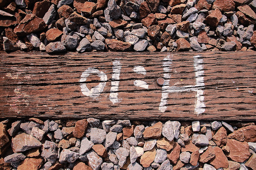 Weathered wooden railway sleeper with white painted markings on gravel