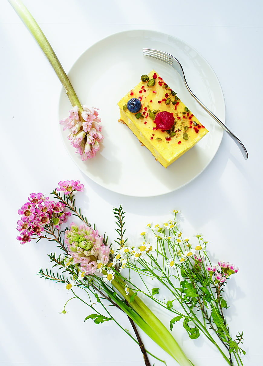 Yellow dessert slice with berries and flowers on white plate