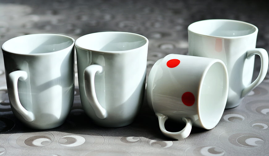 White Porcelain Mugs With Red Dots On Patterned Tablecloth