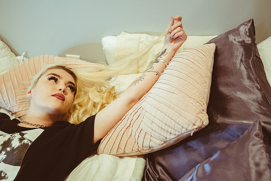 Blonde woman with tattoos relaxing on bed with pillows
