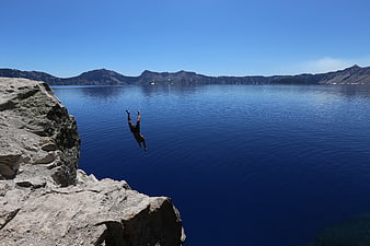 Man cliff diving into deep blue crater lake