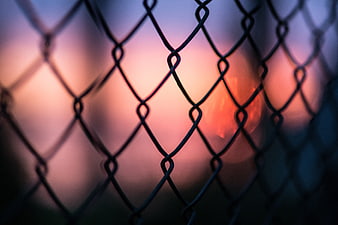 Chain Link Fence Silhouette Against Blurred Sunset Bokeh
