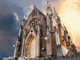 Gothic stone church facade in Gozo, Malta under dramatic sunset sky