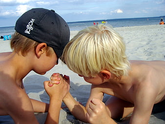 Two young boys arm wrestling on a sandy beach