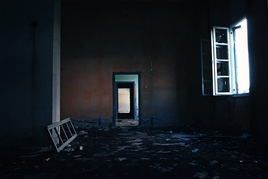 Dark abandoned room with debris and open window
