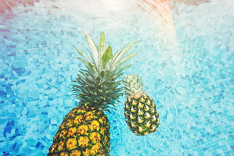 Two pineapples floating in a blue swimming pool
