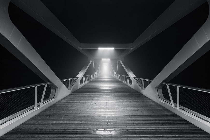 Black and white perspective of a modern wooden bridge at night