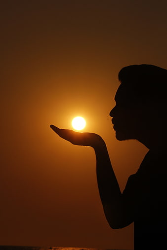 Silhouette of man holding sun in palm at sunset
