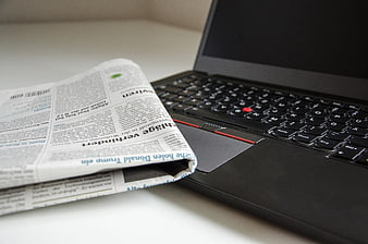 German newspaper and black laptop on white desk