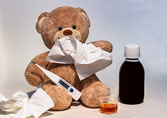Sick teddy bear with thermometer, tissues, and medicine bottle