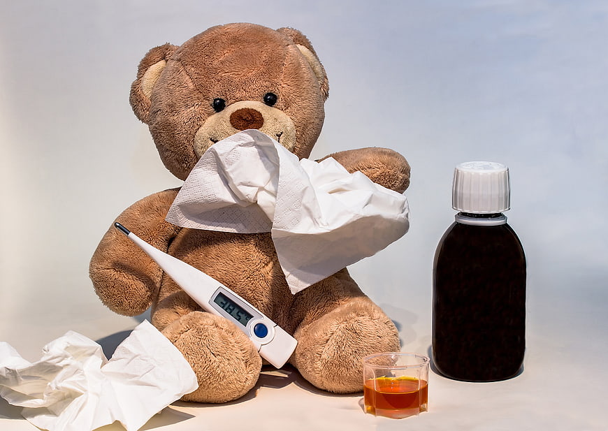 Sick teddy bear with thermometer, tissues, and medicine bottle