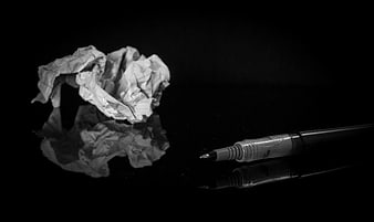 Crumpled paper ball and pen on black reflective surface