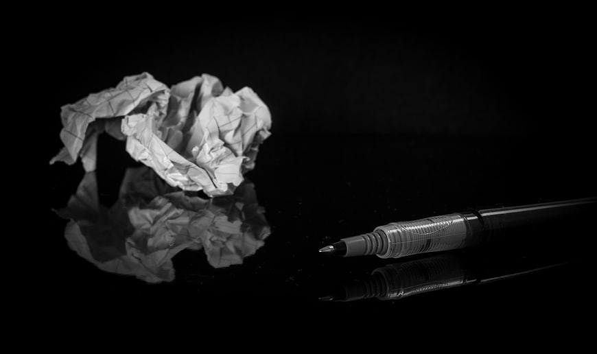 Crumpled paper ball and pen on black reflective surface