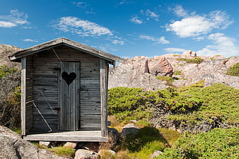Rustic wooden outhouse with heart cutout in rocky landscape