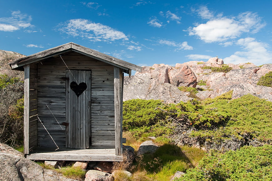 Rustic wooden outhouse with heart cutout in rocky landscape