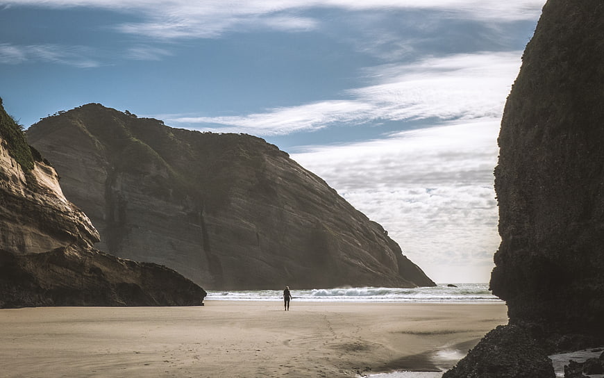 Lone Figure Walking on Sandy Beach Between Cliffs