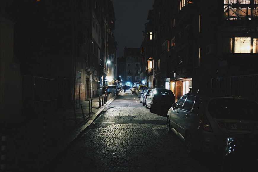 Dark Cobblestone Street at Night with Parked Cars