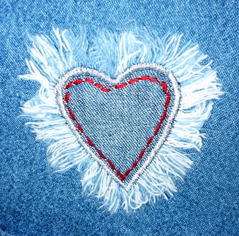 Close-up of distressed denim heart patch with red stitching and frayed edges