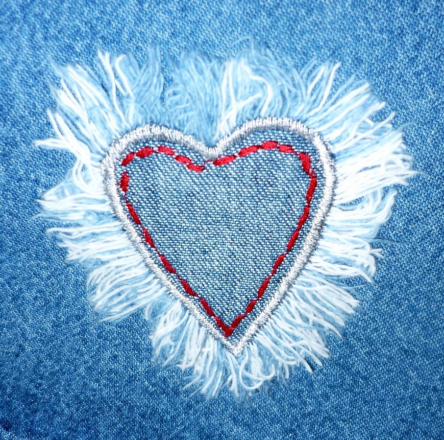 Close-up of distressed denim heart patch with red stitching and frayed edges