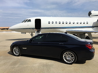 Black luxury sedan parked in front of private jet on airport tarmac