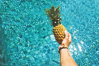 Hand Holding Pineapple Over Blue Pool Water