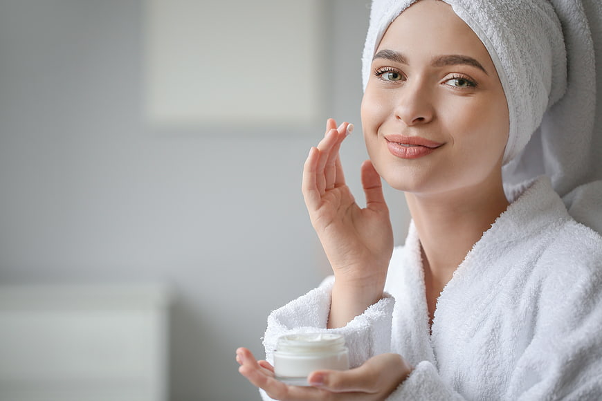 Woman applying face cream with towel on head