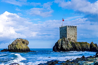 Historic stone tower on rocky island with red flag