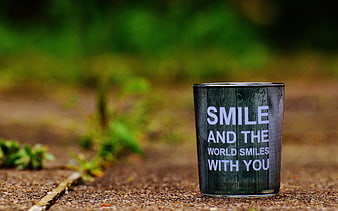 Dark glass tumbler with inspirational smile quote on outdoor stone surface