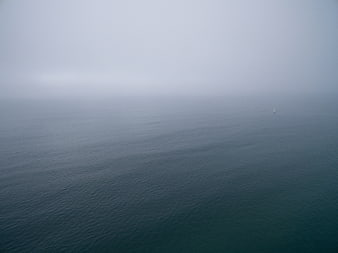 Minimalist foggy ocean seascape with distant sailboat
