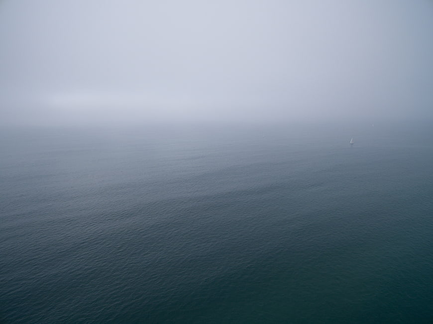 Minimalist foggy ocean seascape with distant sailboat