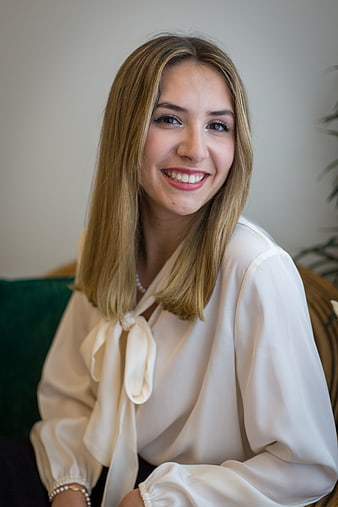 Smiling blonde woman in white blouse sitting indoors