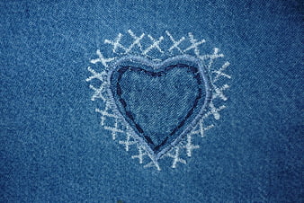 Close-up of embroidered heart on blue denim fabric texture