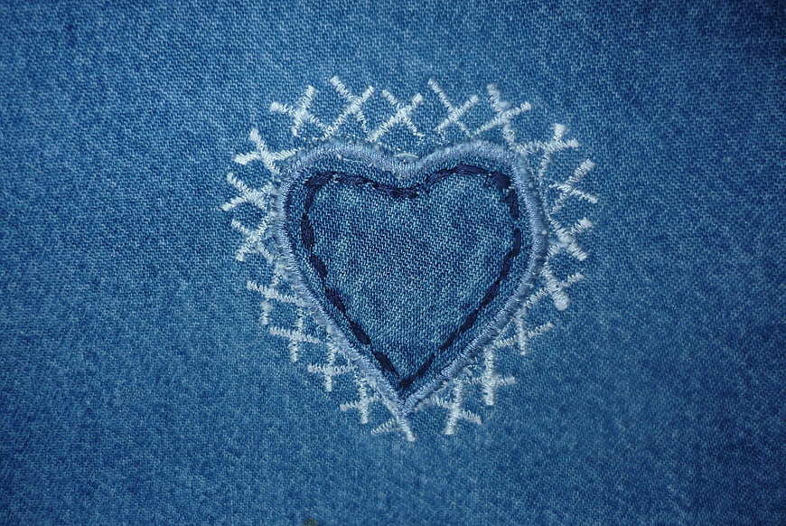 Close-up of embroidered heart on blue denim fabric texture