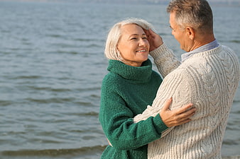 Happy Senior Couple Embracing by the Sea in Winter Sweaters