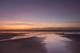 Serene Sunset Seascape with Wet Sand Reflections and Distant Figures